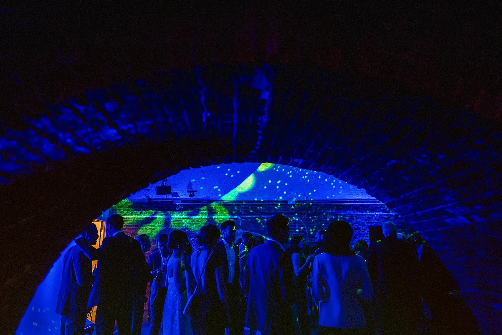 Guests under a brick archway lit by blue and green projections at Hoxton Sessions